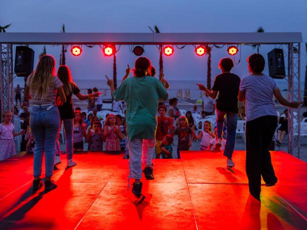 Children dancing on a lit stage at sunset on the beach.