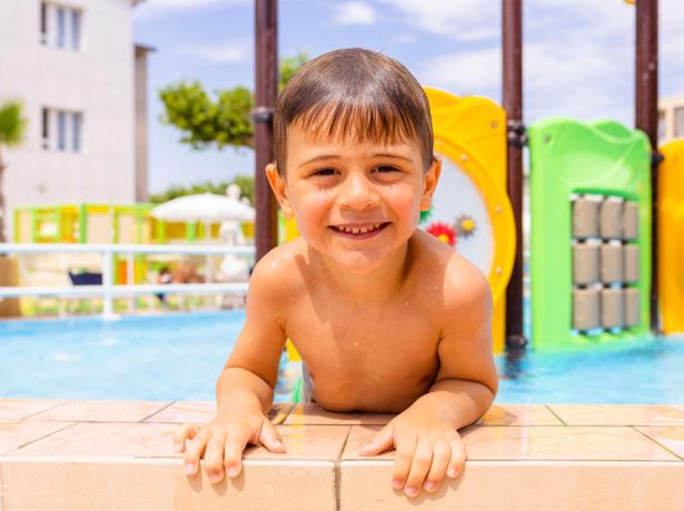 Smiling child in a pool with colorful playground.